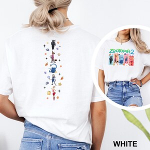 May include: White t-shirt featuring a colorful graphic of characters from "Zootopia 2" on the front. The back of the shirt has a vertical design with cartoon characters and stars. The word "WHITE" is at the bottom.