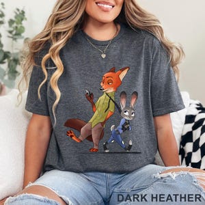 May include: Dark heather gray t-shirt featuring a cartoon illustration of a fox and a rabbit. The fox is holding a phone and the rabbit is walking. The text "DARK HEATHER" is at the bottom of the shirt.