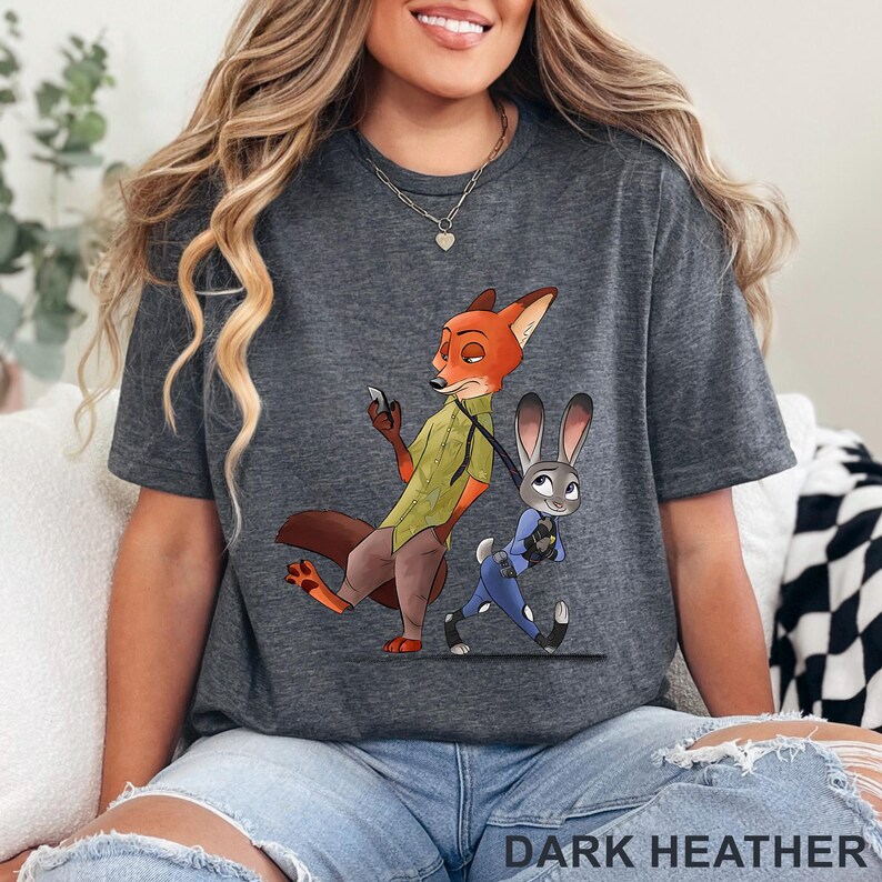 May include: Dark heather gray t-shirt featuring a cartoon illustration of a fox and a rabbit. The fox is holding a phone and the rabbit is walking. The text "DARK HEATHER" is at the bottom of the shirt.