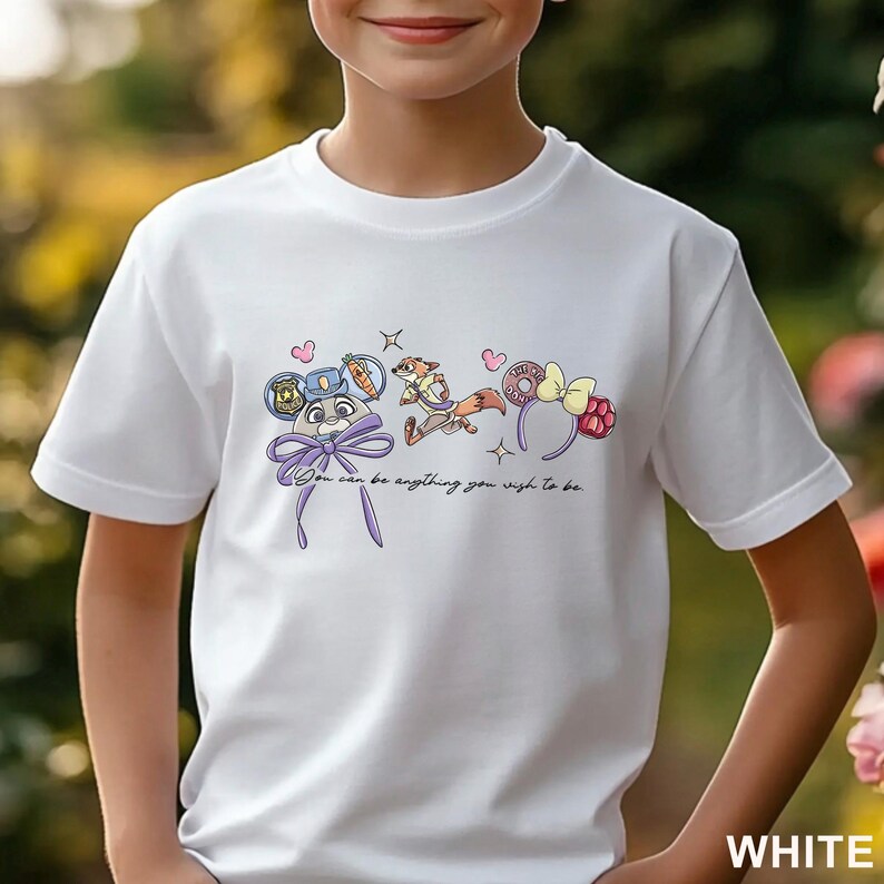 May include: A white short-sleeved t-shirt featuring a graphic print of two cartoon characters, a police badge, a donut, and two sets of ears with bows. The text "You can be anything you wish to be" is printed in black cursive script below the illustrations.