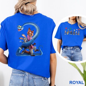 K&ouml;nnte beinhalten: K&ouml;nigsblaues T-Shirt mit einem Cartoon-Motiv einer Schlange, die sich um einen Fuchs und ein Kaninchen windet. Der Fuchs tr&auml;gt einen rosa Anzug und das Kaninchen ein blaues Hemd. Die Grafik befindet sich auf der R&uuml;ckseite des Shirts.