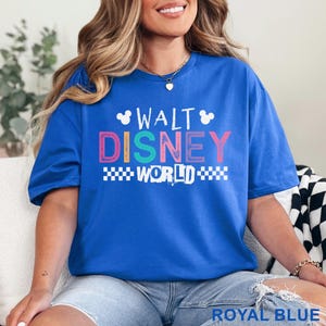 Pu&ograve; includere: Una t-shirt a maniche corte blu reale con la scritta bianca WALT DISNEY WORLD e due piccole sagome della testa di Topolino. La parola DISNEY &egrave; stampata in lettere maiuscole multicolori e la parola WORLD &egrave; affiancata da motivi a scacchiera.
