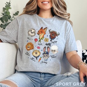 Puede incluir: Una camiseta gris claro con un estampado gr&aacute;fico de varios personajes animales animados, incluyendo un zorro, un conejo, un perezoso y un le&oacute;n. El dise&ntilde;o incluye iconos peque&ntilde;os como una rosquilla, una zanahoria y una placa policial con nombres.