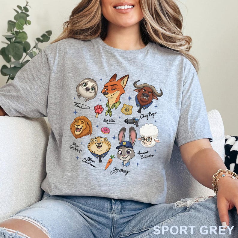 Puede incluir: Una camiseta gris claro con un estampado gr&aacute;fico de varios personajes animales animados, incluyendo un zorro, un conejo, un perezoso y un le&oacute;n. El dise&ntilde;o incluye iconos peque&ntilde;os como una rosquilla, una zanahoria y una placa policial con nombres.