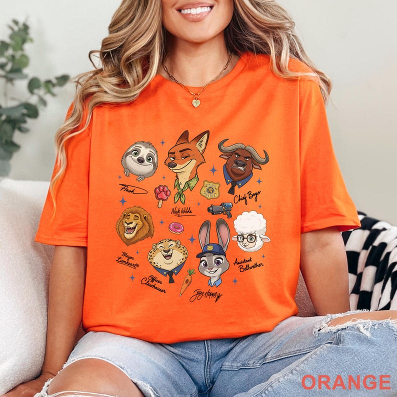 Puede incluir: Una camiseta naranja con un estampado gr&aacute;fico de varios personajes animales animados, incluyendo un zorro, un conejo, un perezoso y un le&oacute;n. El dise&ntilde;o incluye iconos peque&ntilde;os como un d&oacute;nut, una zanahoria y una insignia, con nombres escritos a mano.