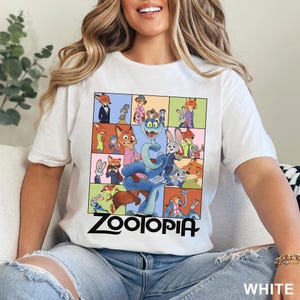 May include: A white short-sleeved t-shirt featuring a multi-paneled graphic print of various Zootopia characters, including a large blue snake in the centre. The word Zootopia is printed in bold black lettering beneath the colourful character grid.
