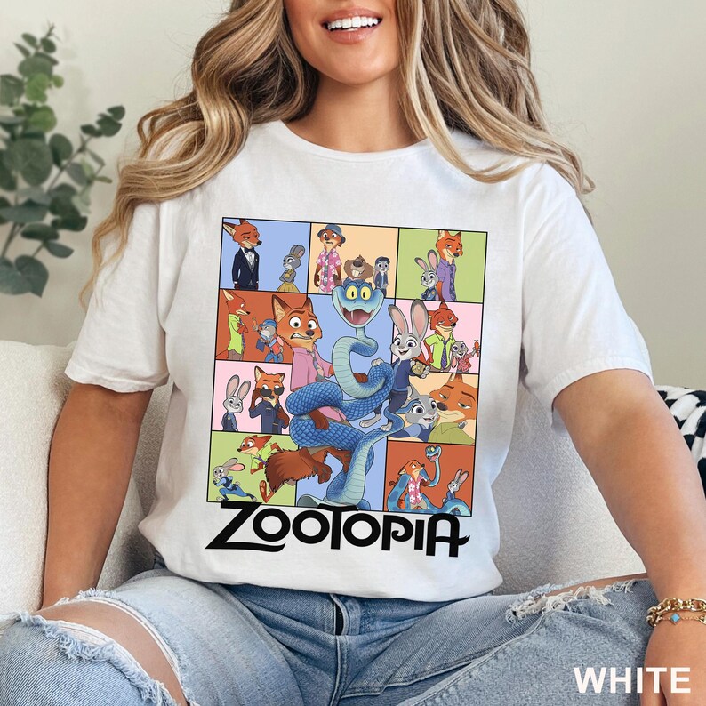 May include: A white short-sleeved t-shirt featuring a multi-paneled graphic print of various Zootopia characters, including a large blue snake in the centre. The word Zootopia is printed in bold black lettering beneath the colourful character grid.