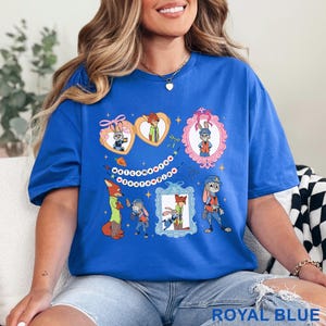 Pode incluir: Camiseta azul royal com personagens de desenhos animados em molduras e formatos de cora&ccedil;&atilde;o. A camiseta tem o texto "Welcome to Zootopia" e &eacute; feita de um material macio.