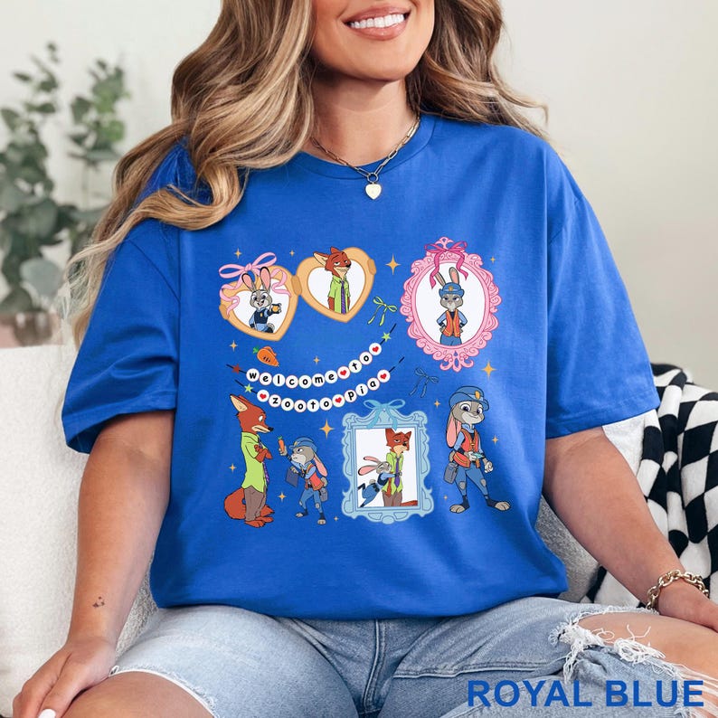 Pode incluir: Camiseta azul royal com personagens de desenhos animados em molduras e formatos de cora&ccedil;&atilde;o. A camiseta tem o texto "Welcome to Zootopia" e &eacute; feita de um material macio.