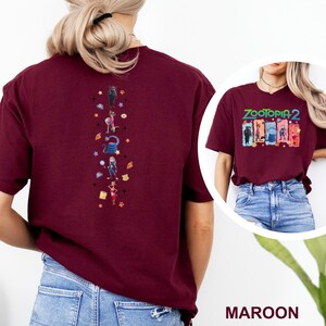 May include: Maroon t-shirt featuring a colorful graphic from Zootopia 2 on the front and a vertical design of characters on the back. The shirt is a solid maroon color and has short sleeves.