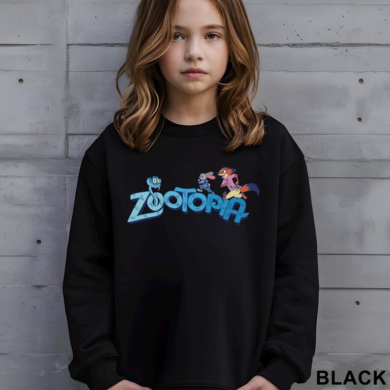 Peut inclure: Sweat-shirt noir avec le mot "Zootopia" en bleu et des personnages de dessins anim&eacute;s. Le mot "BLACK" est imprim&eacute; en blanc en bas &agrave; droite. Le sweat-shirt est port&eacute; par une personne.