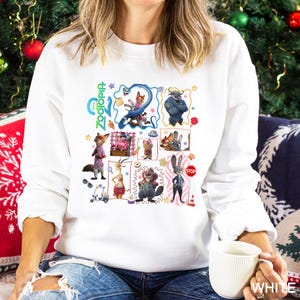 May include: White sweatshirt featuring a colorful graphic of characters from the animated film "Zootopia." The design includes various animal characters in a collage-style arrangement. The word "Zootopia" is written in green and blue script.