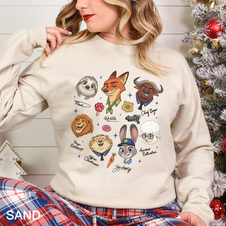May include: A beige sweatshirt featuring cartoon characters from the movie Zootopia. The characters include Flash, Nick Wilde, Chief Bogo, Mayor Lionheart, Officer Clawhauser, Judy Hopps, and Assistant Bellwether. The word "SAND" is printed at the bottom.
