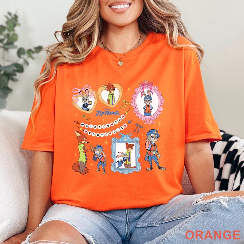 Pode incluir: Camiseta laranja brilhante com ilustra&ccedil;&otilde;es de desenhos animados do filme Zootopia. O design inclui retratos de personagens emoldurados, a palavra "Zootopia" e a frase "Welcome to Zootopia".