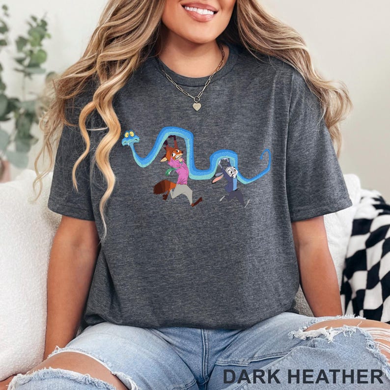 May include: A dark heather gray short-sleeve t-shirt featuring a graphic print of a long blue snake winding above a cartoon fox wearing a pink shirt and a cartoon rabbit wearing a blue uniform. The fabric has a textured, speckled appearance.
