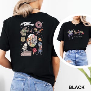 May include: A black t-shirt featuring Zootopia character graphics on the back and front. The back displays a collage of characters, a donut, a badge, and the text "You can be whatever you wish to be." The front shows smaller character icons.