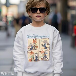 Puede incluir: Sudadera blanca con un gr&aacute;fico de personajes de la pel&iacute;cula de Disney Zootr&oacute;polis. La sudadera tiene el texto "Walt Disney World" en escritura azul encima del gr&aacute;fico. El gr&aacute;fico incluye im&aacute;genes de Nick Wilde y Judy Hopps.