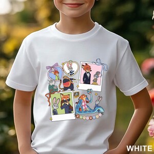 May include: A white short-sleeved t-shirt featuring a graphic print of Zootopia characters in various frames and polaroid-style photos, including Nick Wilde and Judy Hopps, with the text Zootopia displayed in colorful circular icons at the bottom.