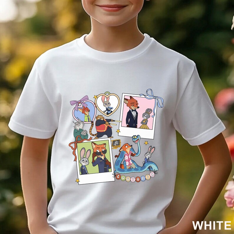 May include: A white short-sleeved t-shirt featuring a graphic print of Zootopia characters in various frames and polaroid-style photos, including Nick Wilde and Judy Hopps, with the text Zootopia displayed in colorful circular icons at the bottom.
