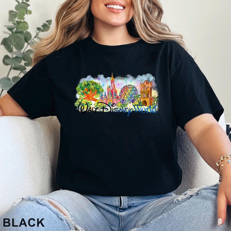 May include: A black short-sleeve t-shirt featuring a colorful graphic print of the Walt Disney World theme park landmarks, including the castle and geodesic sphere, with the text Walt Disney World printed in a blue script font across the center.