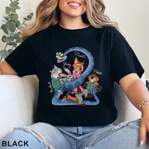Puede incluir: Una camiseta negra con un estampado gr&aacute;fico de varios personajes animados, incluyendo un zorro, un conejo, un gato, un castor y una serpiente. El dise&ntilde;o incluye los textos Pawbert, Judy, Nick y Nibbles escritos en estilo cursivo.