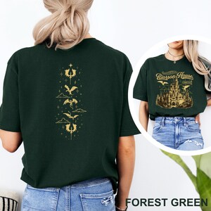 May include: Forest green t-shirt with a gold dragon design on the back. The front of the shirt has a circular image with the text "Rioroson House Castle" and a castle graphic. The shirt is made of a soft material.