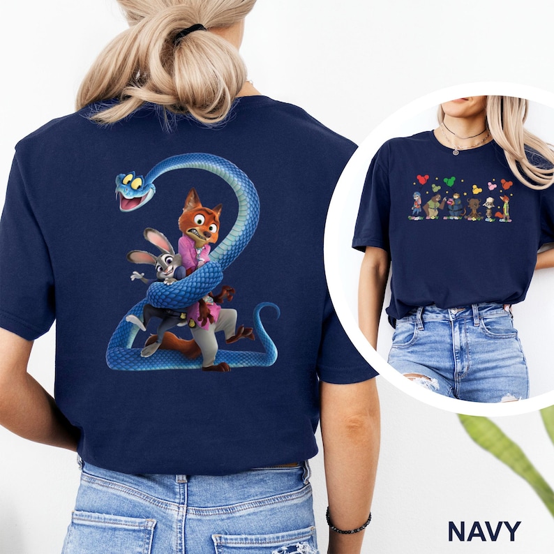 K&ouml;nnte beinhalten: Marineblaues T-Shirt mit einem farbenfrohen Motiv von Charakteren aus dem Film Zootopia, darunter Judy Hopps und Nick Wilde, verschlungen mit einer blauen Schlange. Ein kleineres Motiv von Zootopia-Charakteren ist ebenfalls vorhanden. Das Wort "NAVY" ist unten aufgedruckt.