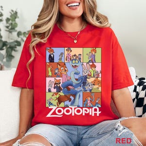 May include: A bright red t-shirt featuring a large graphic print of various characters from the movie Zootopia, including a central blue snake, with the word Zootopia printed in white lettering at the bottom of the colourful character collage.