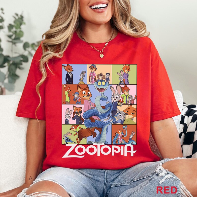 May include: A bright red t-shirt featuring a large graphic print of various characters from the movie Zootopia, including a central blue snake, with the word Zootopia printed in white lettering at the bottom of the colourful character collage.