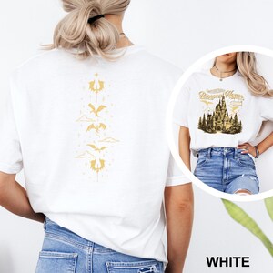 May include: White t-shirt with a gold dragon design on the back. The design features a series of dragons and cloud shapes. The front of the shirt has a graphic of a castle with the text "Disney Home".