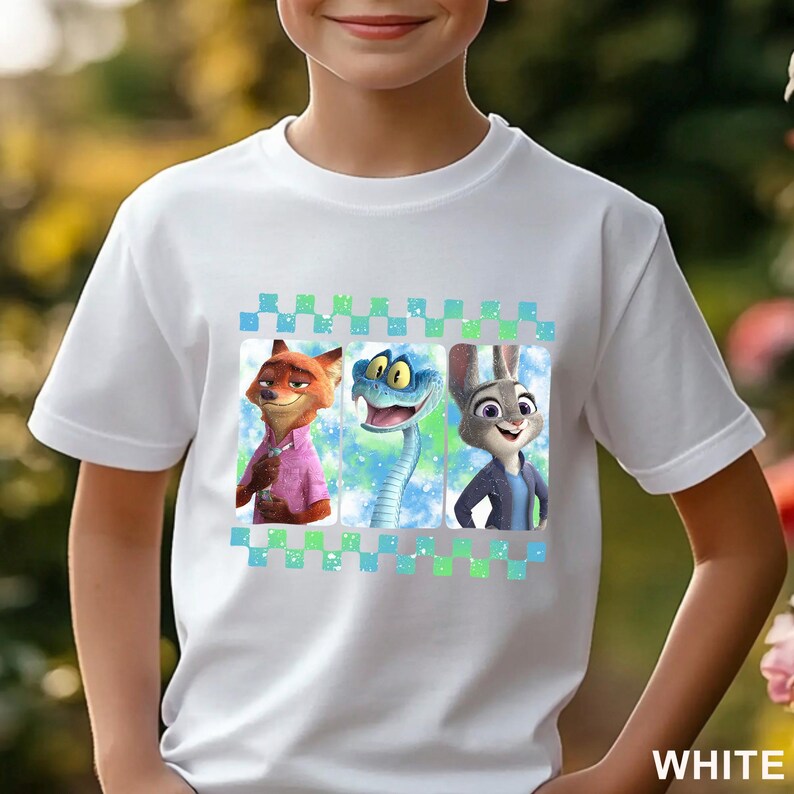 May include: White t-shirt featuring three cartoon characters: a fox in a pink shirt, a snake, and a rabbit in a blue jacket. The design is set against a blue and green background with a checkered border. The word "WHITE" is printed at the bottom.