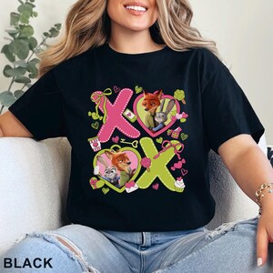 Peut inclure: Un t-shirt noir avec une impression graphique affichant le texte XOXO, des c&oelig;urs roses et vert citron, ainsi que des illustrations de Nick Wilde et Judy Hopps de Zootopie. Le motif inclut des ic&ocirc;nes comme un caf&eacute;, une cl&eacute; et des cadeaux.