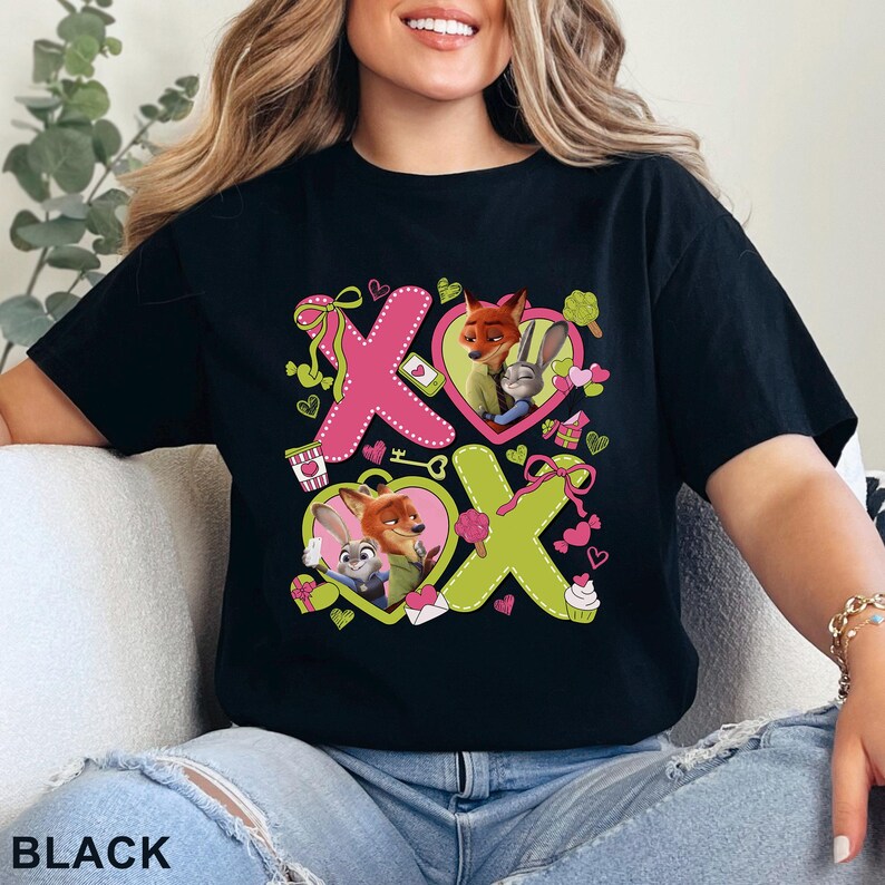 Peut inclure: Un t-shirt noir avec une impression graphique affichant le texte XOXO, des c&oelig;urs roses et vert citron, ainsi que des illustrations de Nick Wilde et Judy Hopps de Zootopie. Le motif inclut des ic&ocirc;nes comme un caf&eacute;, une cl&eacute; et des cadeaux.