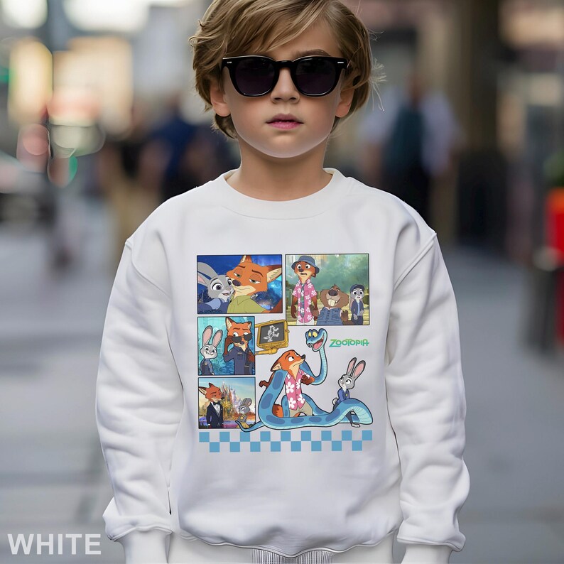 May include: White sweatshirt featuring a colorful comic strip design with characters from the animated movie "Zootopia." The design includes images of a fox, a rabbit, and other characters. The word "Zootopia" is also visible.