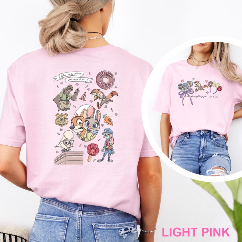 May include: A light pink t-shirt featuring a Zootopia-themed graphic on the back with characters like Nick Wilde and Judy Hopps, a donut, a badge, and the text "You can be whatever you wish to be." The front shows a smaller matching graphic.