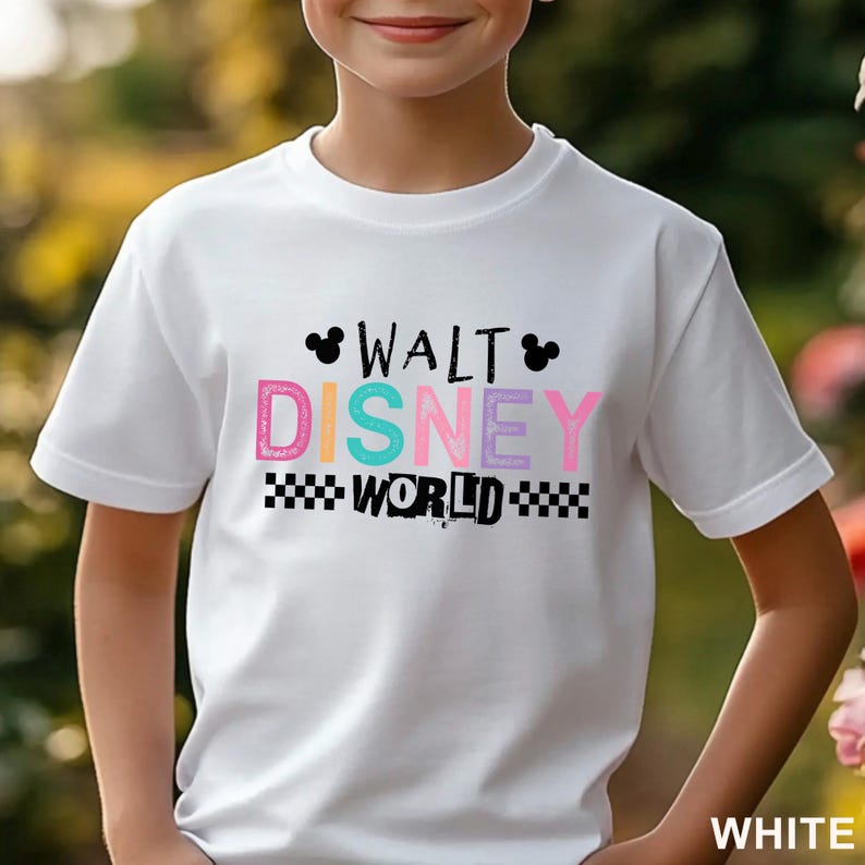 Pu&ograve; includere: Una t-shirt bianca a maniche corte con la scritta WALT DISNEY WORLD in lettere nere e colorate. Il design include due piccole sagome nere di orecchie di Topolino e un motivo a scacchi bianco e nero sotto la parola WORLD.