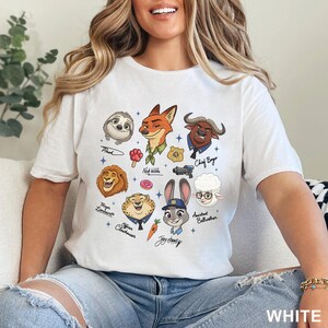Puede incluir: Una camiseta blanca con un estampado gr&aacute;fico de varios personajes animados de Zootr&oacute;polis, incluyendo a Nick Wilde, Judy Hopps, Chief Bogo, Flash, Mayor Lionheart, Officer Clawhauser y Assistant Bellwether, junto con peque&ntilde;os iconos como un helado de pata, un donut, una zanahoria y una placa.