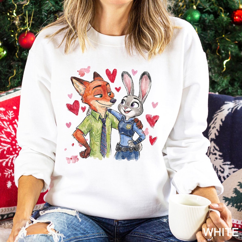 May include: White sweatshirt with a watercolour illustration of Nick Wilde and Judy Hopps from Zootropolis, surrounded by red hearts. Nick is a fox in a green shirt and tie, and Judy is a bunny in a police uniform. A themed apparel item.