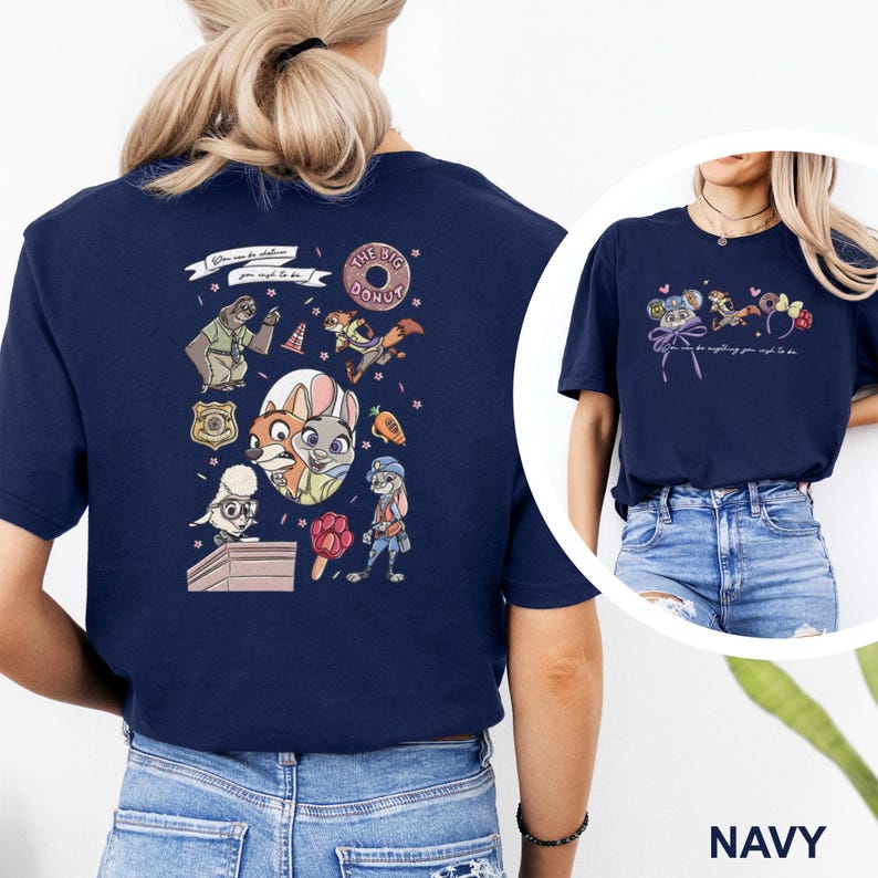 May include: A navy blue t-shirt featuring a Zootopia-themed graphic print. The back displays various characters, a badge, a donut, and a carrot, with the text "You can be whatever you wish to be." The front shows smaller character icons and ears.