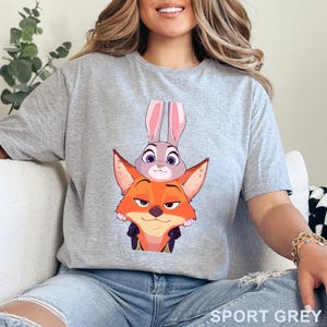 May include: Sport grey t-shirt with a cartoon illustration of Judy Hopps the bunny and Nick Wilde the fox from Zootropolis. The characters are stacked. The text "SPORT GREY" is printed at the bottom.