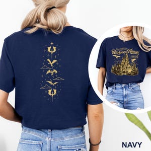 May include: Navy blue t-shirt with a gold dragon and castle design. The back of the shirt features a vertical arrangement of gold dragons and symbols. The front displays the text "Riorson House" above a castle illustration.