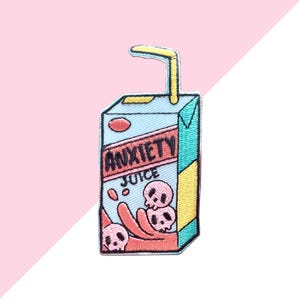 May include: Embroidered patch featuring a juice box design with the words "ANXIETY JUICE". The patch is light blue with a red rectangle and the word "ANXIETY" in black. The juice box has a yellow straw and a pink background.