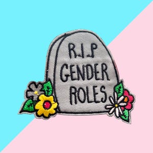May include: Embroidered patch featuring a gray tombstone with the text "R.I.P. GENDER ROLES" in black. The tombstone is decorated with colorful flowers, including yellow, white, and red blooms, set against a blue and pink background.