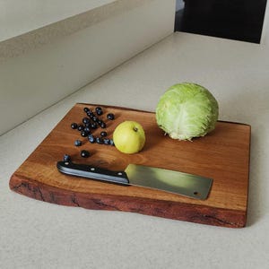 May include: A wooden cutting board with a live edge, a knife, a green head of lettuce, a green apple, and blueberries.