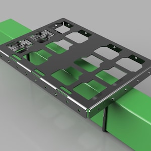 May include: A dark gray metal bracket with a rectangular shape and cut-out sections, resting on two bright green rectangular supports. The bracket has multiple holes and is designed for mounting or securing other components. The background is a light gray.