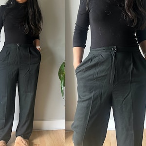 Könnte beinhalten: Schwarze Hose mit hohem Bund, Knopfverschluss und Falten. Die Hose hat ein gerades Bein-Design und Taschen. Die Hose ist aus einem dunklen Stoff gefertigt. Das Model trägt ein schwarzes Langarm-Top.