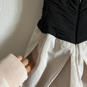K&ouml;nnte beinhalten: Ein schwarz-wei&szlig;es Kleid mit einem plissierten Rock und einem gerafften Oberteil. Das Kleid hat eine figurbetonte Silhouette und ein klassisches Design. Das Kleid ist aus leichtem Stoff gefertigt und perfekt f&uuml;r einen besonderen Anlass.