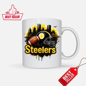 K&ouml;nnte beinhalten: Wei&szlig;e Keramiktasse mit einem Design der Pittsburgh Steelers. Das Design zeigt einen Football, einen schwarzen Helm mit gelbem Stern und eine Stadtlandschaft in Gelb und Schwarz. Das Wort "Steelers" ist gelb.