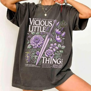 May include: Dark gray oversized t-shirt featuring the text "VICIOUS LITTLE THING" with a sword and floral design in purple and green. The shirt has a vintage, worn look.