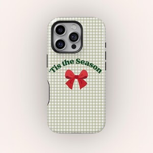 Pode incluir: Uma capa de telefone com um padrão xadrez vichy verde claro e branco. A capa apresenta o texto "'Tis the Season" em verde, com um gráfico de laço vermelho. A capa tem um recorte para a câmera e botões laterais pretos.